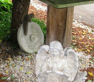 Check it Out! Look how long and full my tail is, how alert my eyes and ears are. I am perched on the sundial (Note: location near the porch) while that beautiful Garden Fairy, hands folded in prayer, is facing the front door so she is protected from the environment each time the door opens. But hey, what gives, look at me, I have praying paws as well, but so far, I still have to scrounge to eat and find shelter. When the world order changes, we will not forget this indignity visited upon the Squirrel Nation,